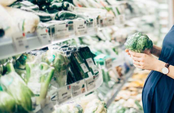 A pregnant woman picks fresh broccoli from the supermarket vegetable aisle.