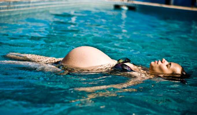 A nine months pregnant woman, wearing a bikini, closes her eyes and floats on her back in a pool.
