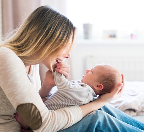 Mother with her newborn baby son sitting on a bed