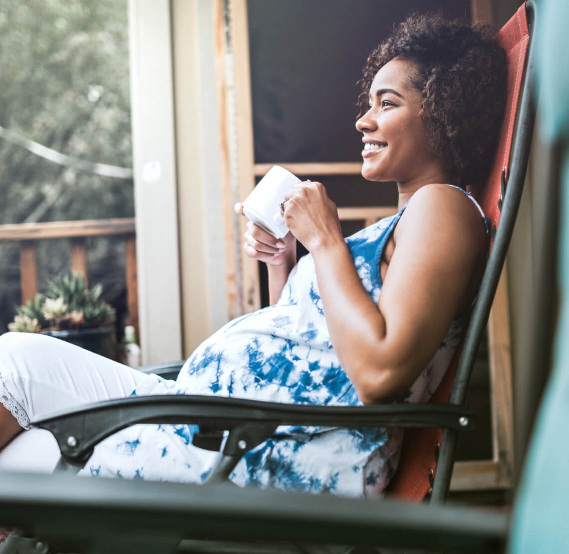 Image of a pregnant woman sitting on a chair and holding a mug.