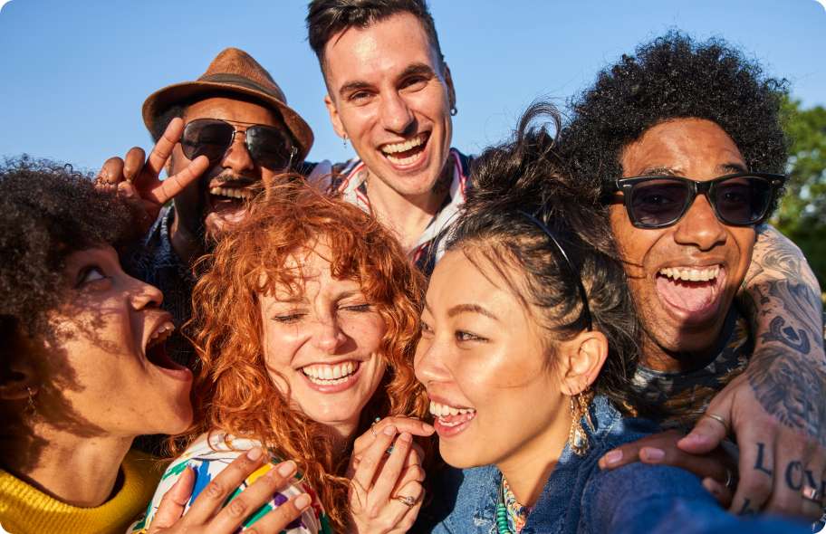 Image of a young group of people from different ethnic backgrounds smiling and laughing in the sun.