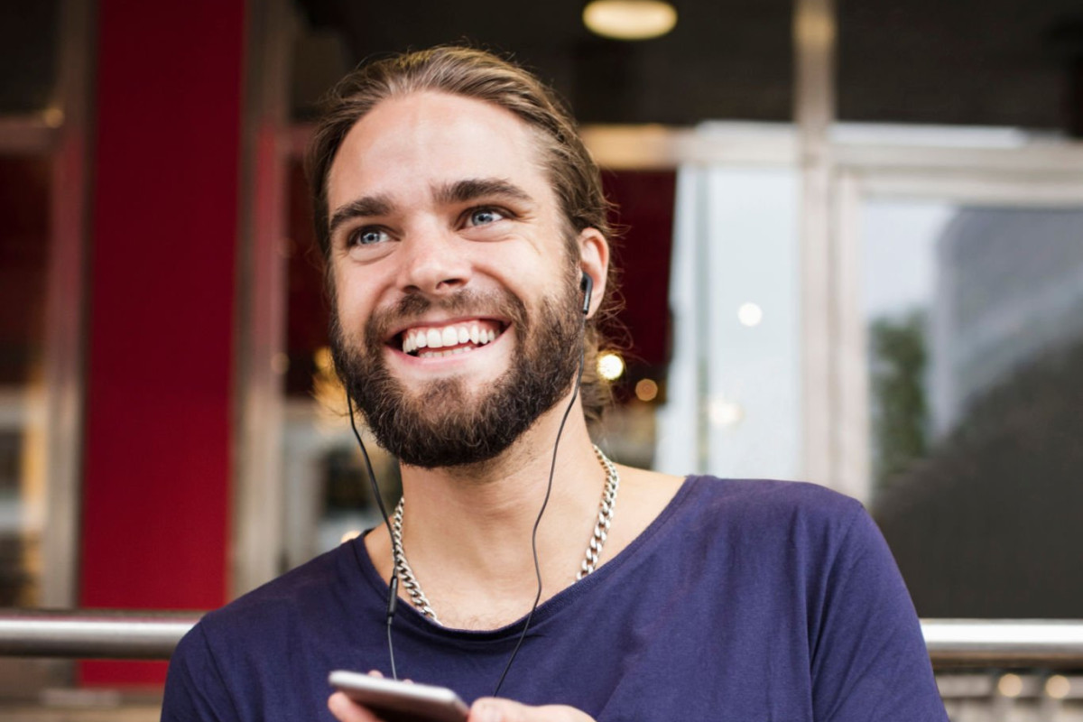 A grown individual wearing earphones, chuckling while listening to something