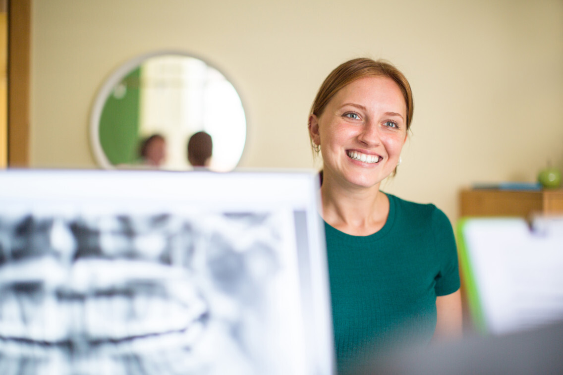 Young woman standing at dental clinic reception desk and smiling.